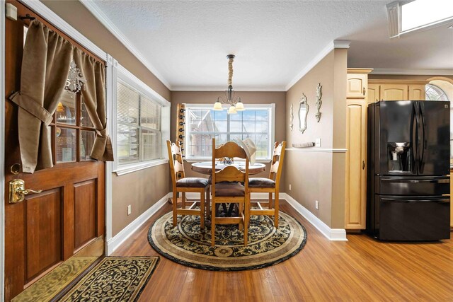 dining space featuring a textured ceiling, ornamental molding, a chandelier, and light hardwood / wood-style flooring