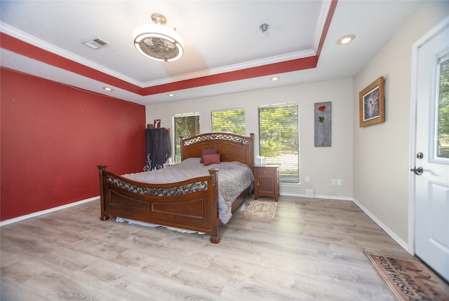 bedroom with light hardwood / wood-style floors, crown molding, and a tray ceiling