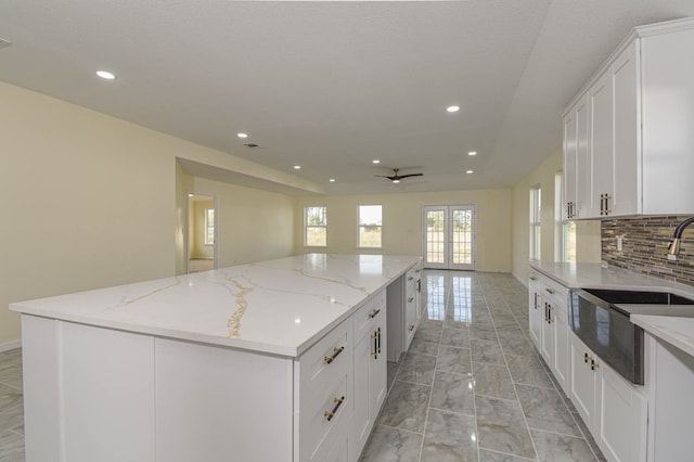 kitchen with white cabinets, light stone countertops, a center island, and backsplash