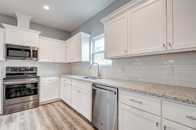 kitchen with decorative backsplash, light stone counters, stainless steel appliances, sink, and white cabinets