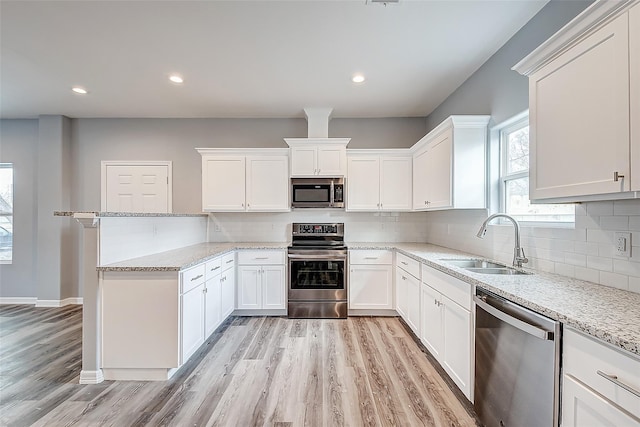 kitchen featuring light stone countertops, appliances with stainless steel finishes, sink, light hardwood / wood-style flooring, and white cabinetry