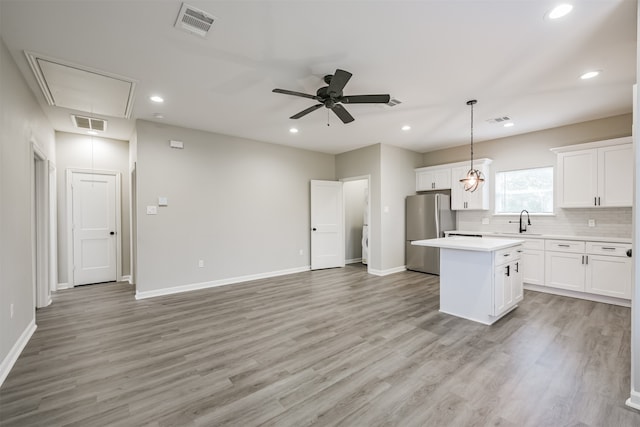 kitchen featuring hanging light fixtures, a center island, light wood-type flooring, white cabinetry, and stainless steel refrigerator