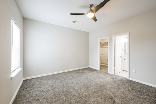 unfurnished bedroom with ensuite bathroom, a walk in closet, a closet, ceiling fan, and light colored carpet