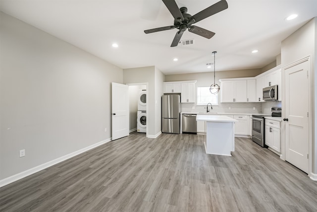 kitchen with stacked washer / drying machine, hanging light fixtures, white cabinetry, light wood-type flooring, and appliances with stainless steel finishes