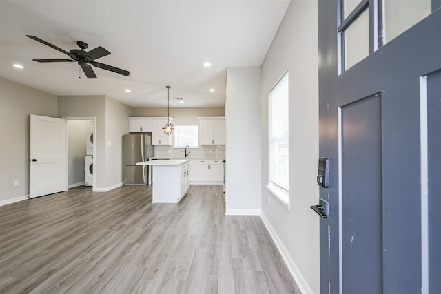 kitchen with white cabinets, stacked washing maching and dryer, plenty of natural light, and stainless steel fridge