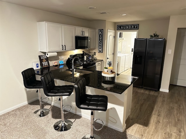 kitchen featuring white cabinets, a breakfast bar, dark stone counters, independent washer and dryer, and black appliances