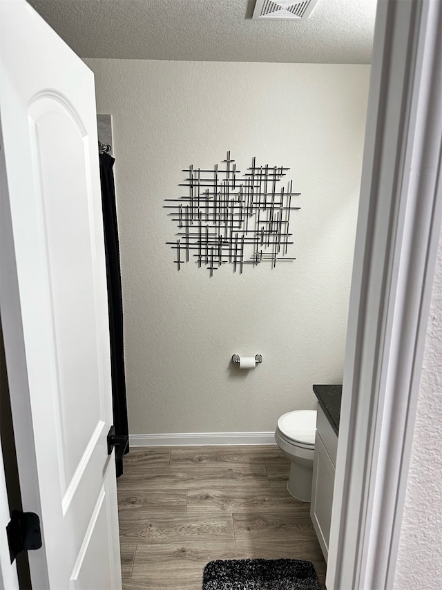 bathroom featuring vanity, a textured ceiling, wood-type flooring, and toilet