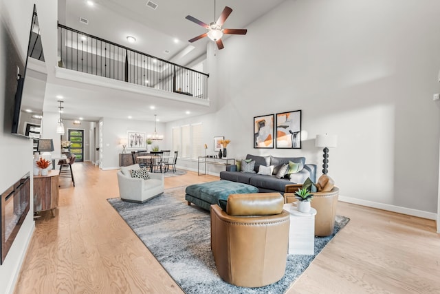 living room featuring ceiling fan, a towering ceiling, and light wood-type flooring