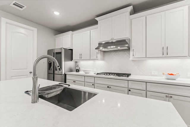 kitchen featuring tasteful backsplash, sink, gas stovetop, white cabinets, and stainless steel refrigerator with ice dispenser