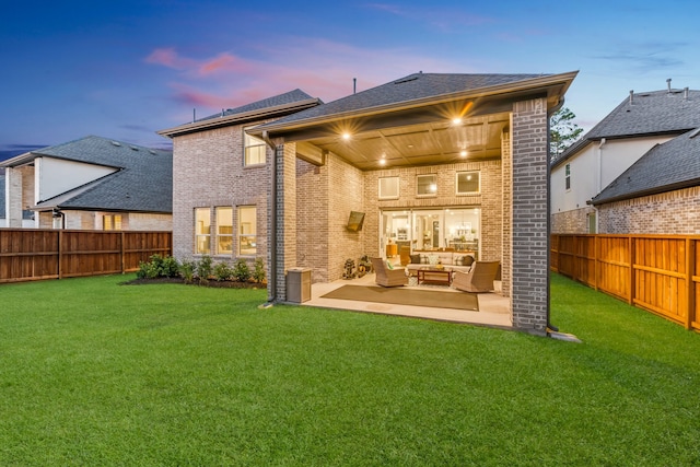 back house at dusk featuring a patio, an outdoor hangout area, and a lawn