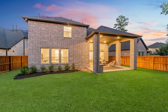 back house at dusk with a patio and a lawn