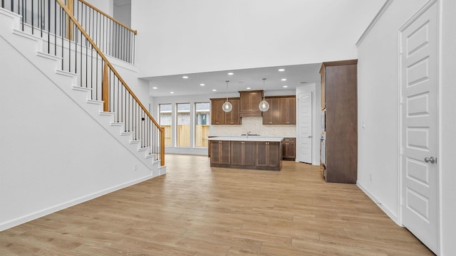 kitchen with light hardwood / wood-style flooring, hanging light fixtures, a towering ceiling, tasteful backsplash, and a kitchen island