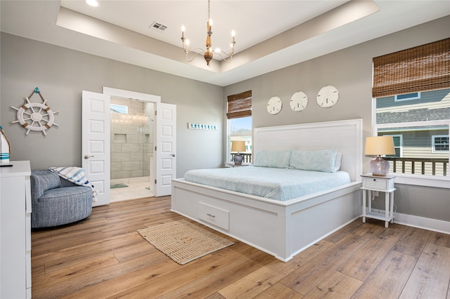 bedroom featuring connected bathroom, a notable chandelier, a tray ceiling, and light hardwood / wood-style flooring