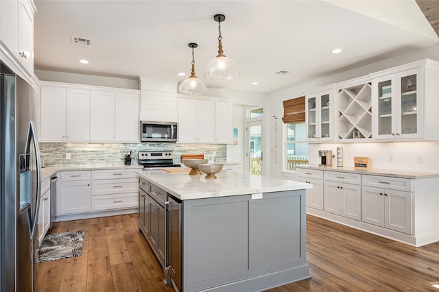 kitchen with white cabinets, hardwood / wood-style floors, a kitchen island, appliances with stainless steel finishes, and pendant lighting