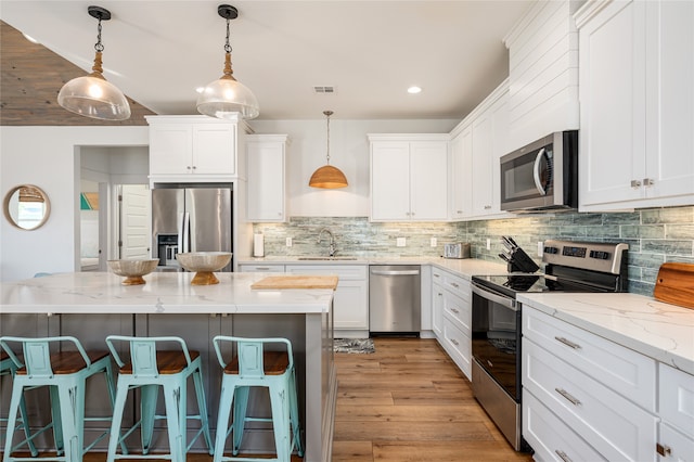 kitchen featuring white cabinets, light stone counters, a kitchen bar, pendant lighting, and stainless steel appliances