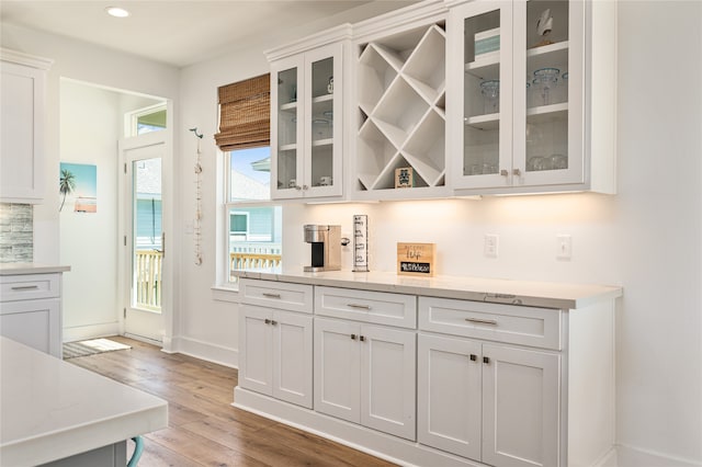 bar with white cabinetry, light hardwood / wood-style floors, and light stone countertops