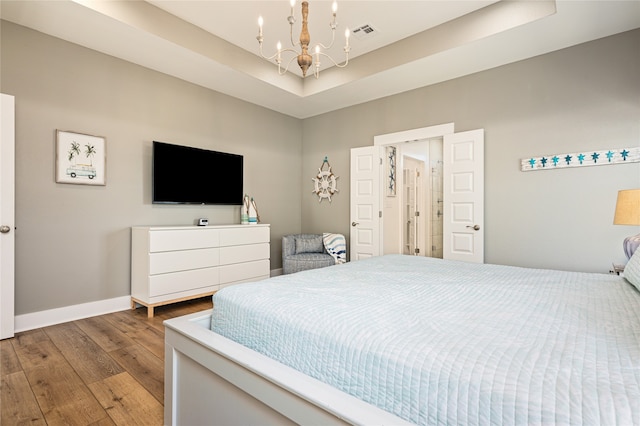 bedroom featuring a notable chandelier, light wood-type flooring, and a raised ceiling