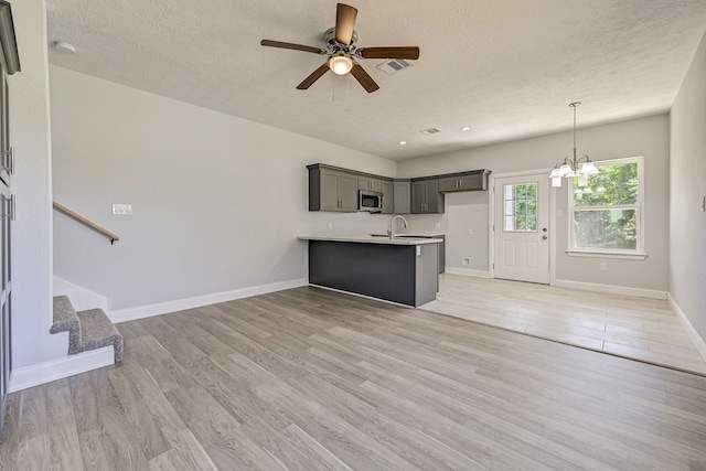 unfurnished living room with a textured ceiling, sink, light wood-type flooring, and ceiling fan with notable chandelier