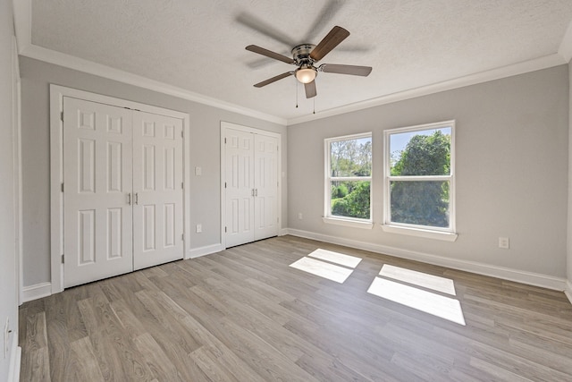 unfurnished bedroom with a textured ceiling, two closets, light wood-type flooring, and ceiling fan