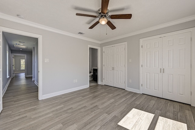 unfurnished bedroom featuring ceiling fan, ornamental molding, light hardwood / wood-style flooring, and two closets