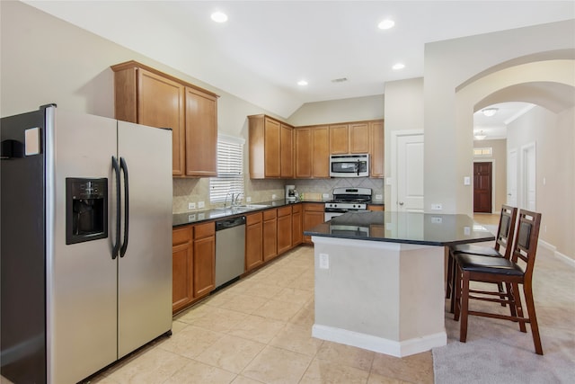 kitchen featuring lofted ceiling, backsplash, light tile patterned flooring, a kitchen bar, and appliances with stainless steel finishes