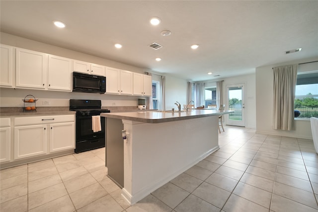 kitchen with black appliances, light tile patterned flooring, a center island with sink, and white cabinets