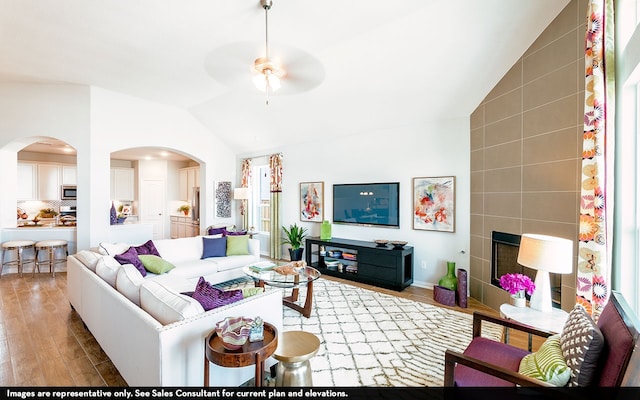 living room featuring a tiled fireplace, ceiling fan, tile walls, vaulted ceiling, and light hardwood / wood-style floors