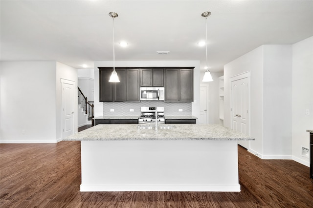 kitchen with dark wood-type flooring, an island with sink, decorative light fixtures, and stainless steel appliances