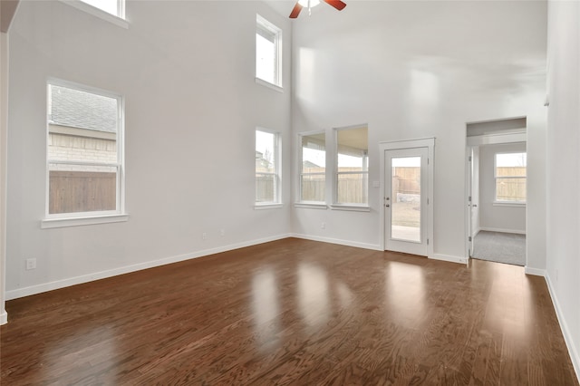 unfurnished living room featuring a wealth of natural light, a high ceiling, dark wood-type flooring, and ceiling fan