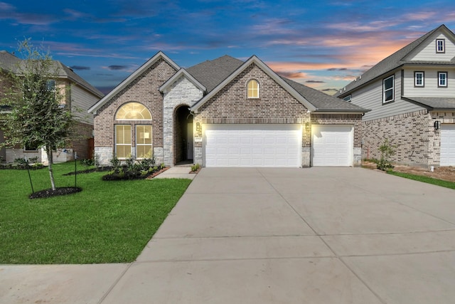 french country inspired facade featuring a front lawn, a garage, driveway, stone siding, and brick siding