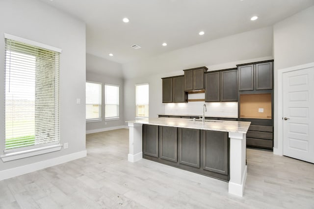 kitchen with an island with sink, vaulted ceiling, backsplash, a sink, and baseboards