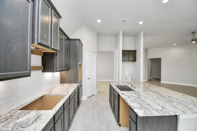kitchen featuring light stone counters, decorative backsplash, light wood-style flooring, a sink, and a ceiling fan