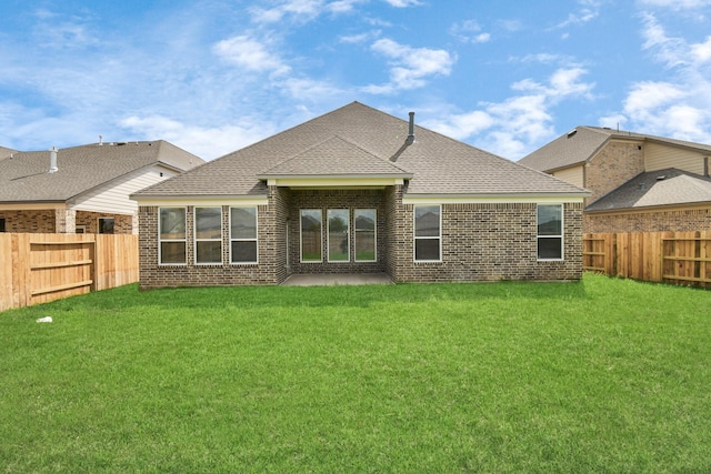 rear view of property featuring a yard, a shingled roof, brick siding, and a fenced backyard