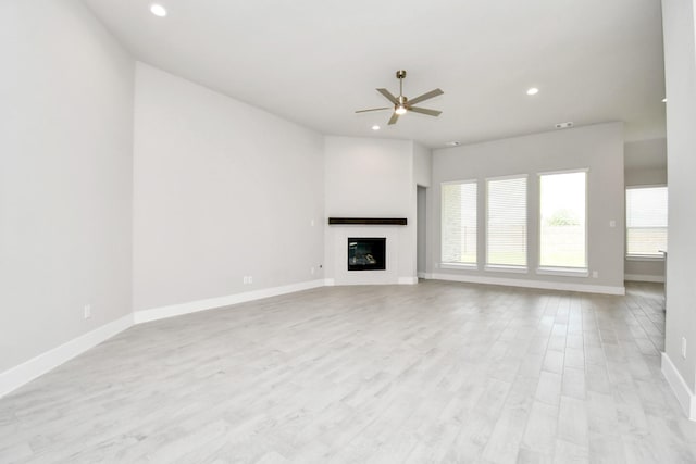 unfurnished living room with ceiling fan, baseboards, a glass covered fireplace, light wood-type flooring, and recessed lighting