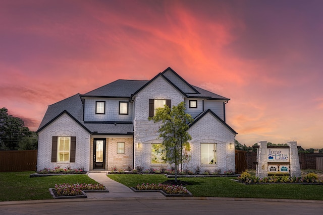view of front of home featuring stone siding, a yard, a shingled roof, and fence