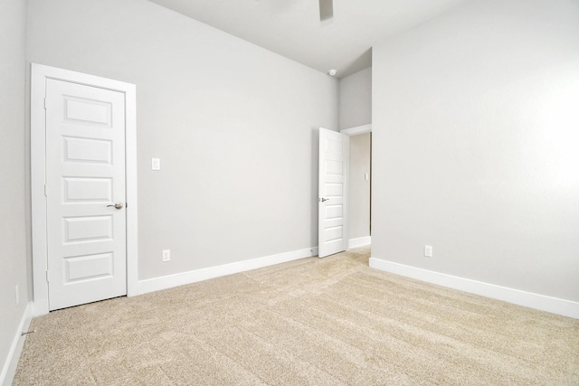 empty room featuring a ceiling fan, baseboards, vaulted ceiling, and light carpet