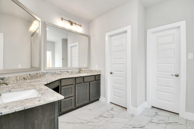 bathroom with baseboards, marble finish floor, double vanity, and a sink