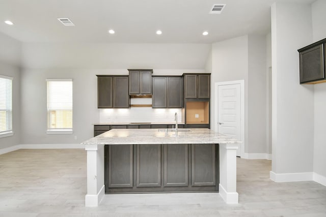 kitchen with a sink, visible vents, light wood-style flooring, baseboards, and an island with sink