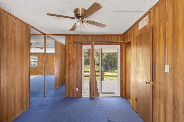 doorway to outside featuring ceiling fan, a textured ceiling, and wooden walls