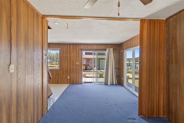 interior space with a textured ceiling, ceiling fan, wooden walls, and carpet floors