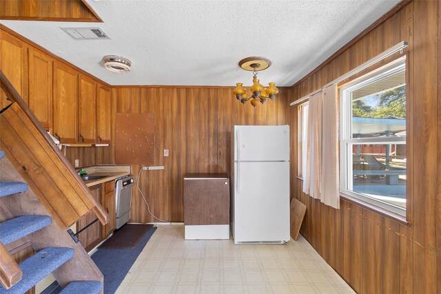 kitchen featuring dishwasher, a textured ceiling, wooden walls, white fridge, and a chandelier