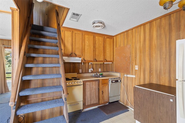 kitchen with white appliances, wood walls, a textured ceiling, and sink