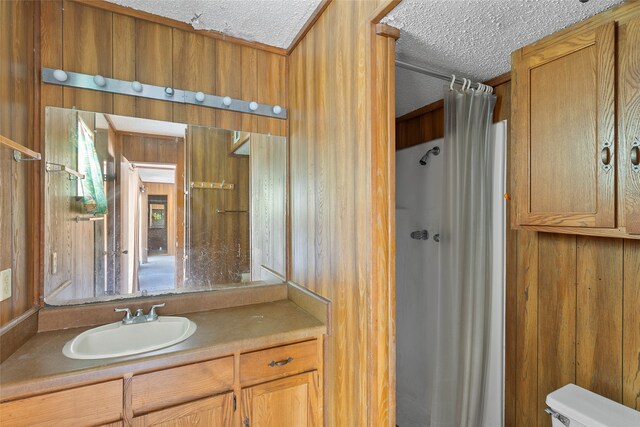 bathroom with toilet, a shower with curtain, vanity, a textured ceiling, and wood walls