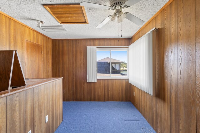 empty room featuring ceiling fan, wood walls, carpet flooring, and a textured ceiling