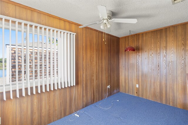 unfurnished bedroom featuring a textured ceiling, ceiling fan, wooden walls, crown molding, and carpet