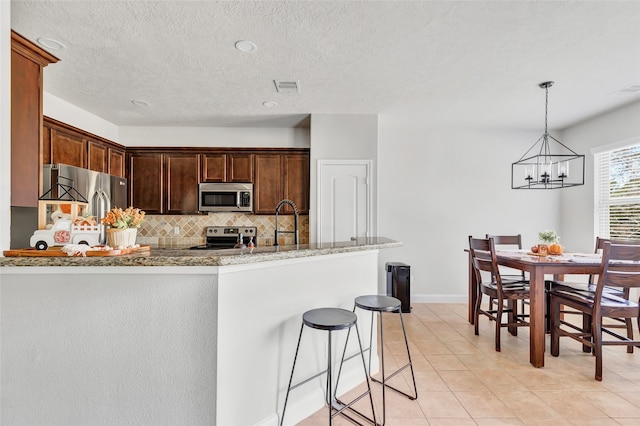 kitchen with tasteful backsplash, appliances with stainless steel finishes, hanging light fixtures, light stone counters, and a notable chandelier