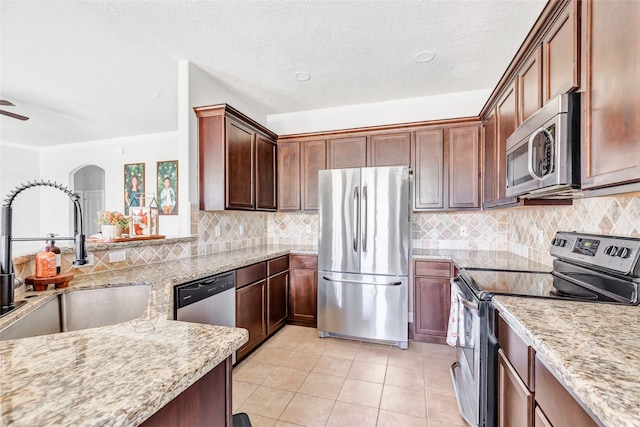 kitchen with backsplash, sink, appliances with stainless steel finishes, light stone counters, and a textured ceiling