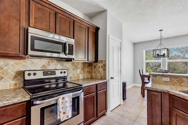 kitchen with stainless steel appliances, backsplash, light stone countertops, an inviting chandelier, and light tile patterned floors