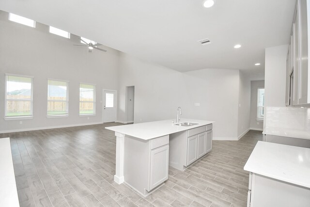 kitchen featuring a towering ceiling, sink, ceiling fan, light hardwood / wood-style floors, and a kitchen island with sink