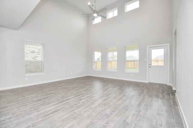 unfurnished living room with light hardwood / wood-style floors, high vaulted ceiling, and ceiling fan